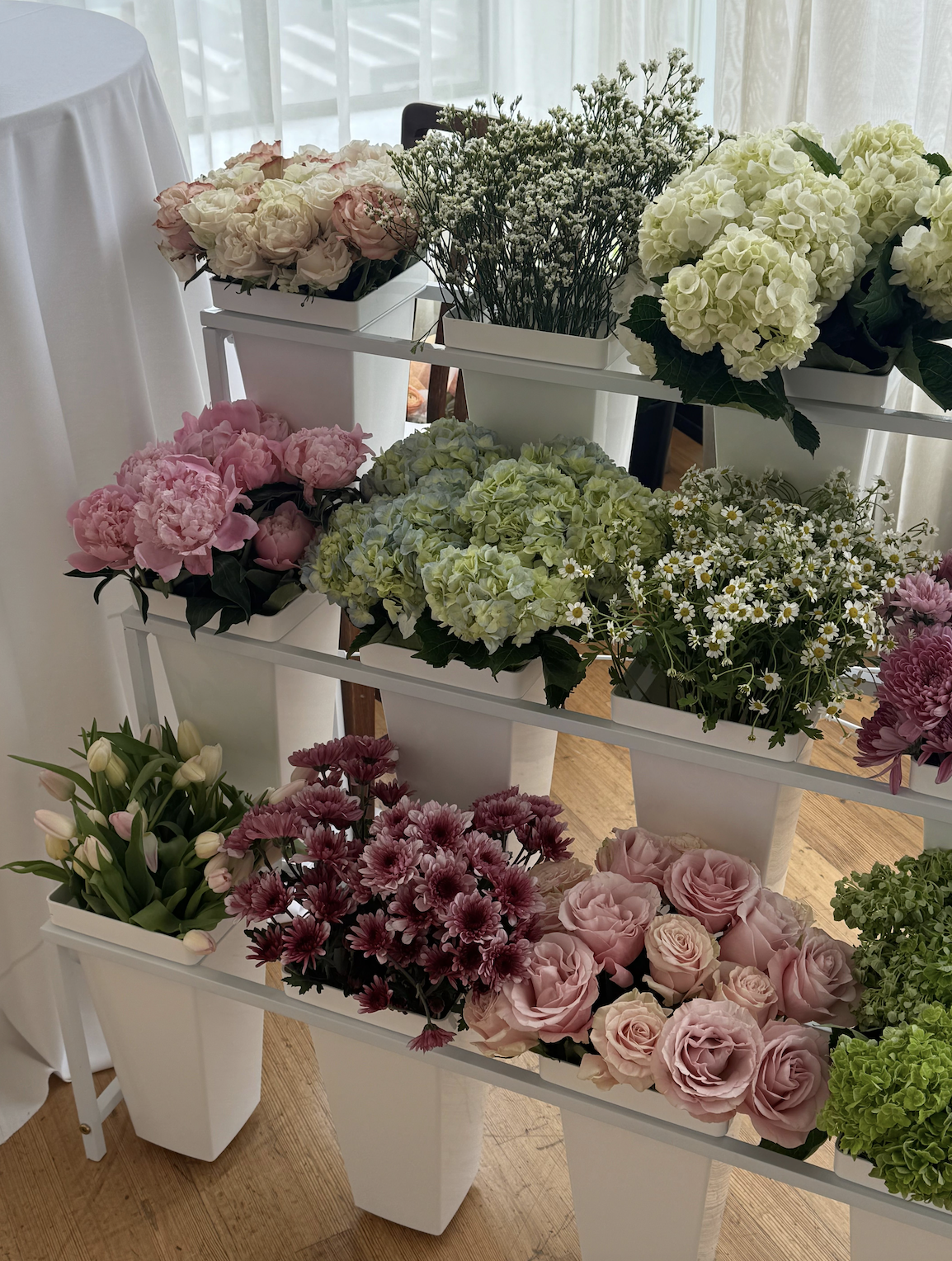Pink roses, peonies, hydrangeas, tulips, and daisies arranged in white buckets for a build-your-own bloom bar.